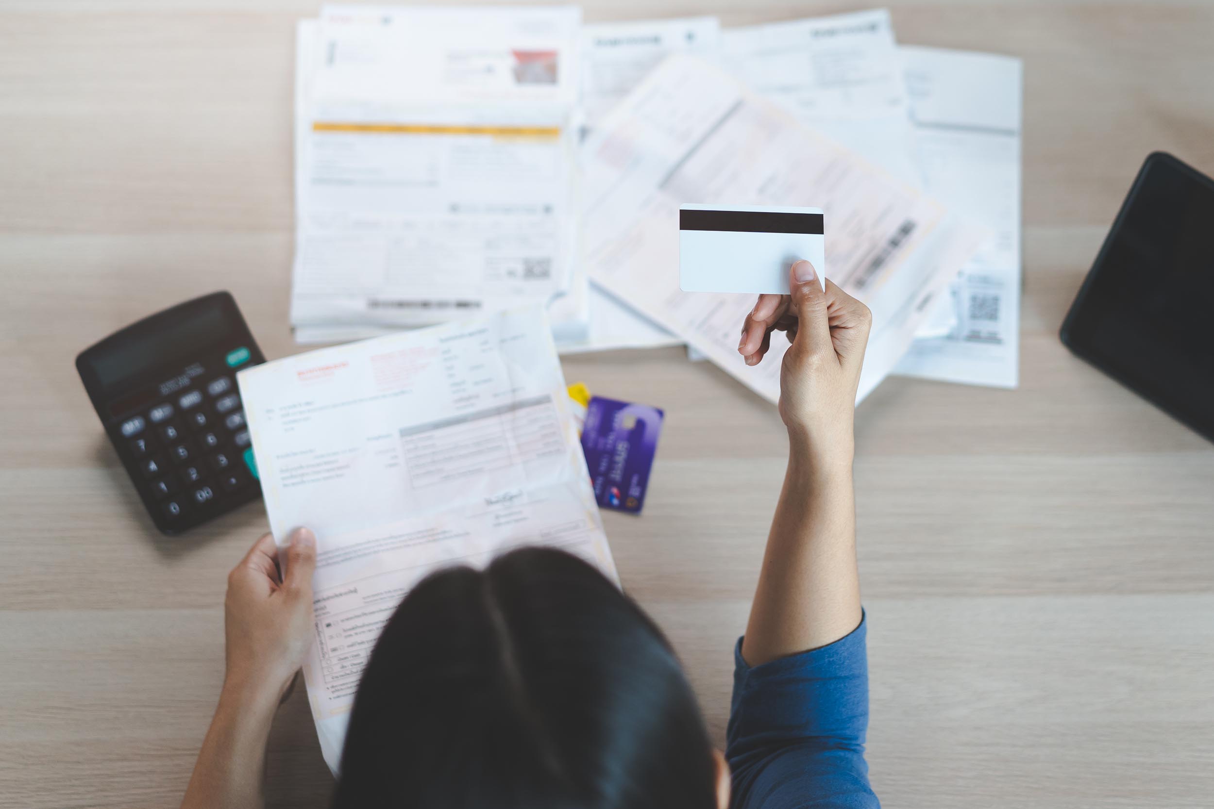 Top view of stressed young asian woman trying to find money to pay credit card debt. Selective focus on hand.